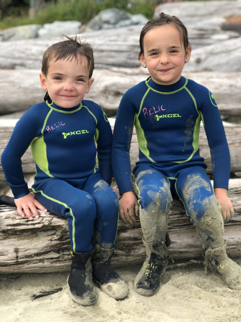 Photo of twins sitting on the beach wearing wetsuits